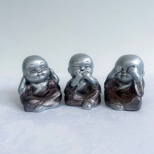 Front view of monk trio, painted silver figures with bronze robes, all sitting in a row.