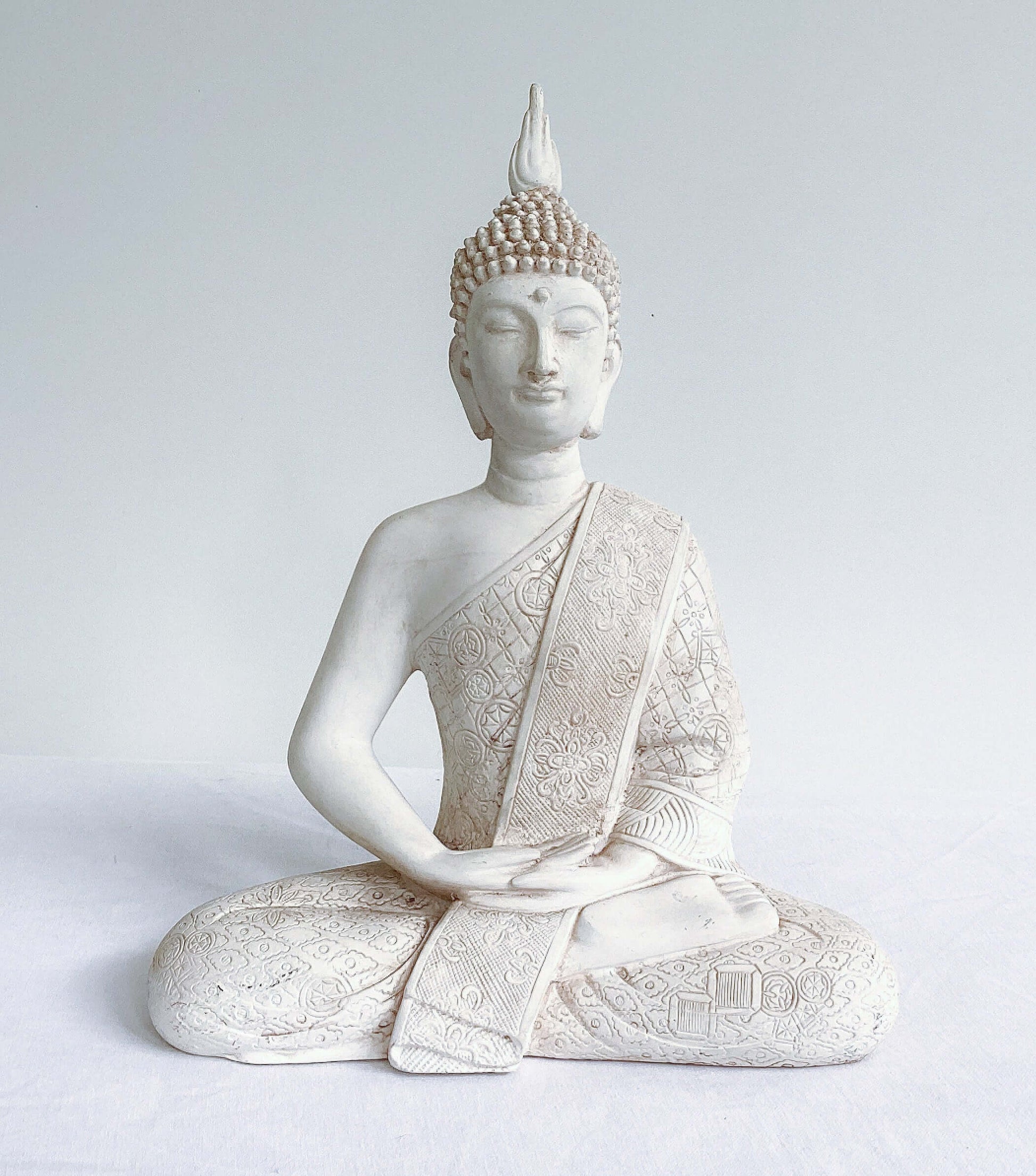 Front view of buddha in lotus position, natural off white coloring, ornate robes, with ushnisha on head.