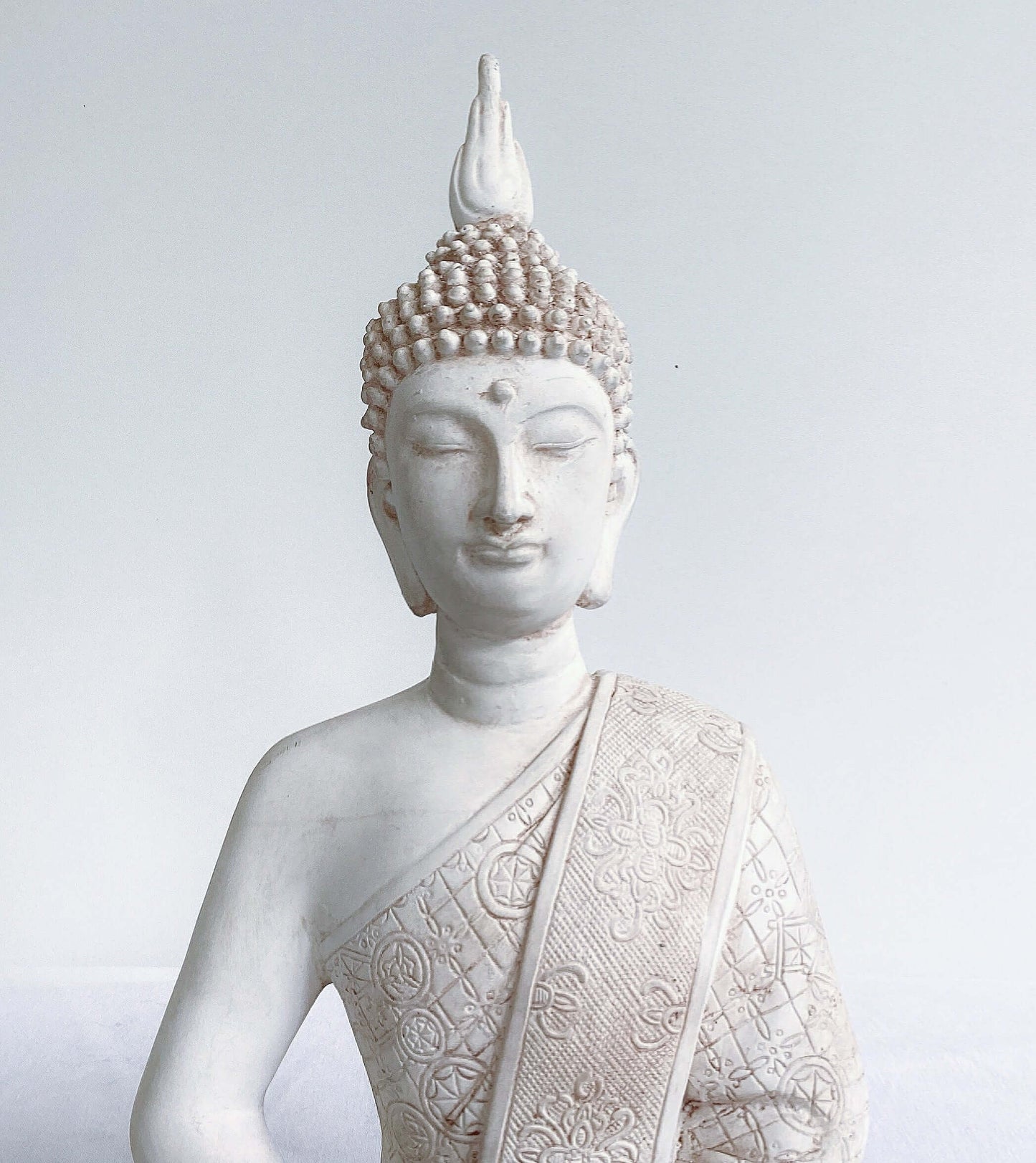 Front detail view of buddha torso, natural off white coloring, ornate robes, with ushnisha on head.