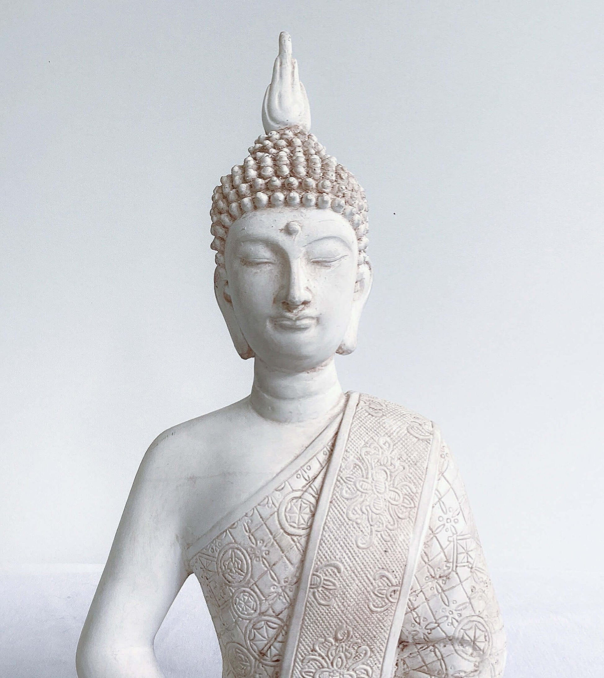 Front detail view of buddha torso, natural off white coloring, ornate robes, with ushnisha on head.