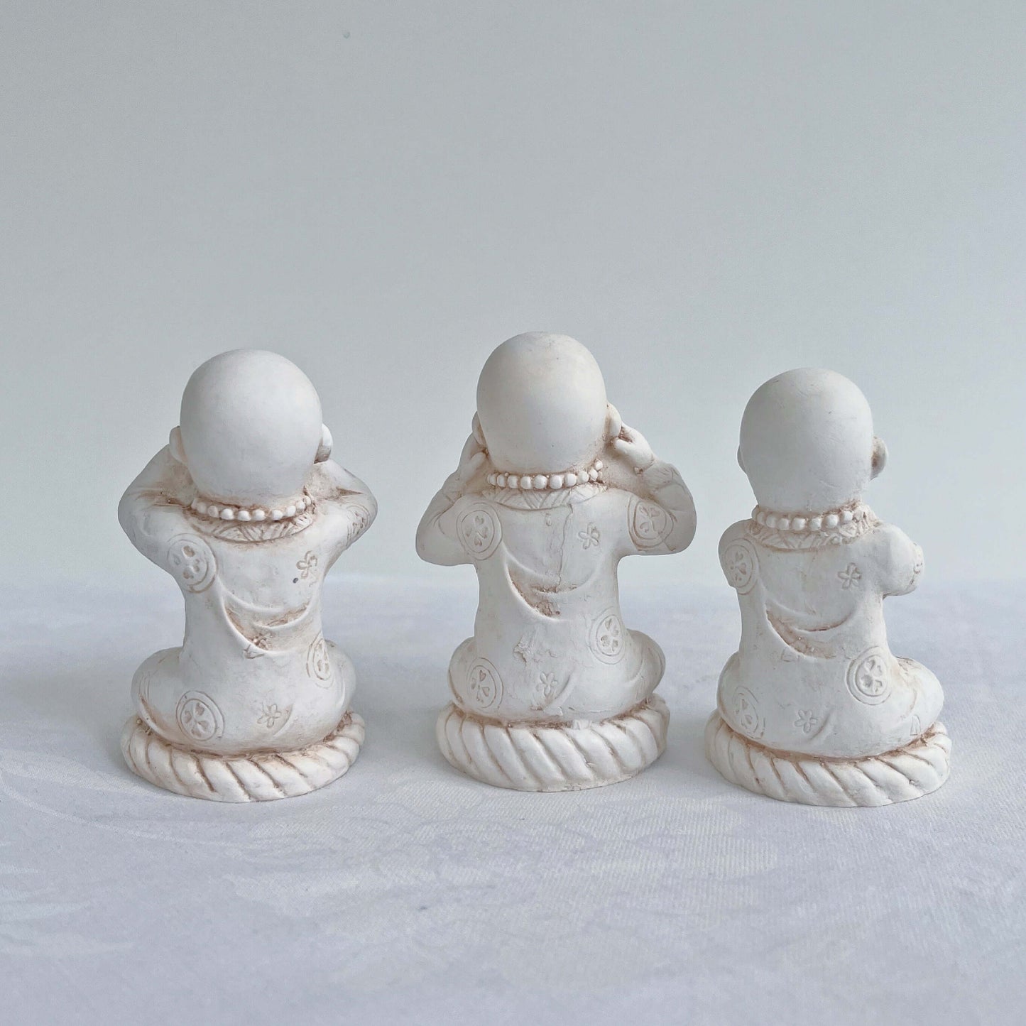 Back view of monks in a row, all natural off white colors, with ornate robes.