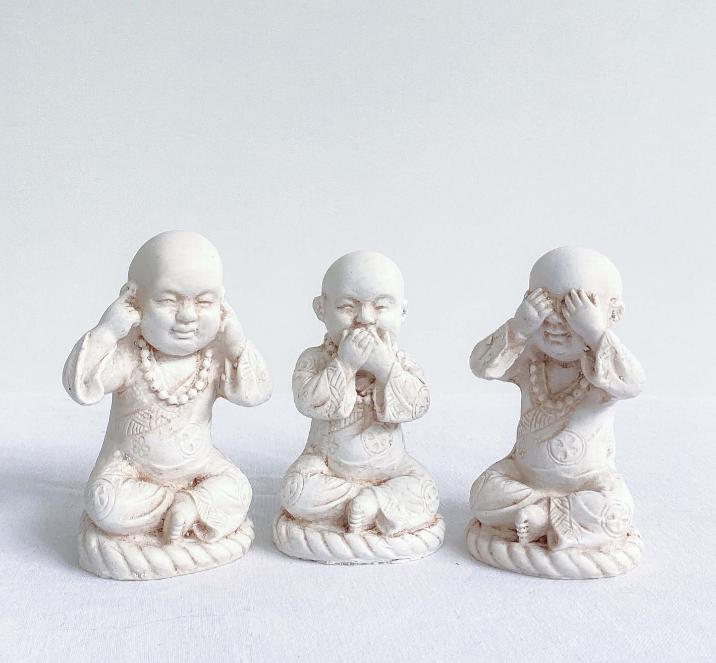 Front view of monks, all three in a row, natural off white colors, with ornate robes.