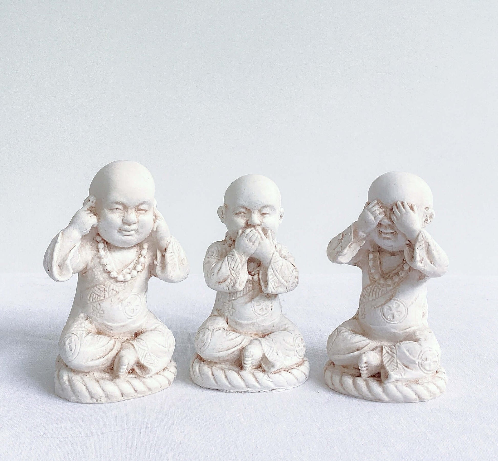 Front view of monks, all three in a row, natural off white colors, with ornate robes.