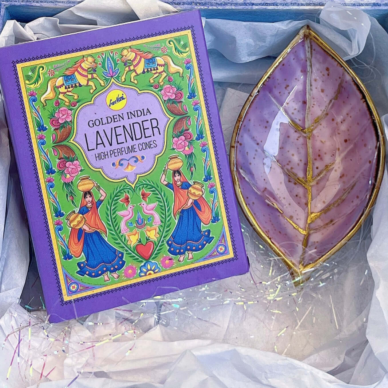 Contents detail view of incense and plum painted ceramic leaf, nestled in white tissue paper and tinsel.