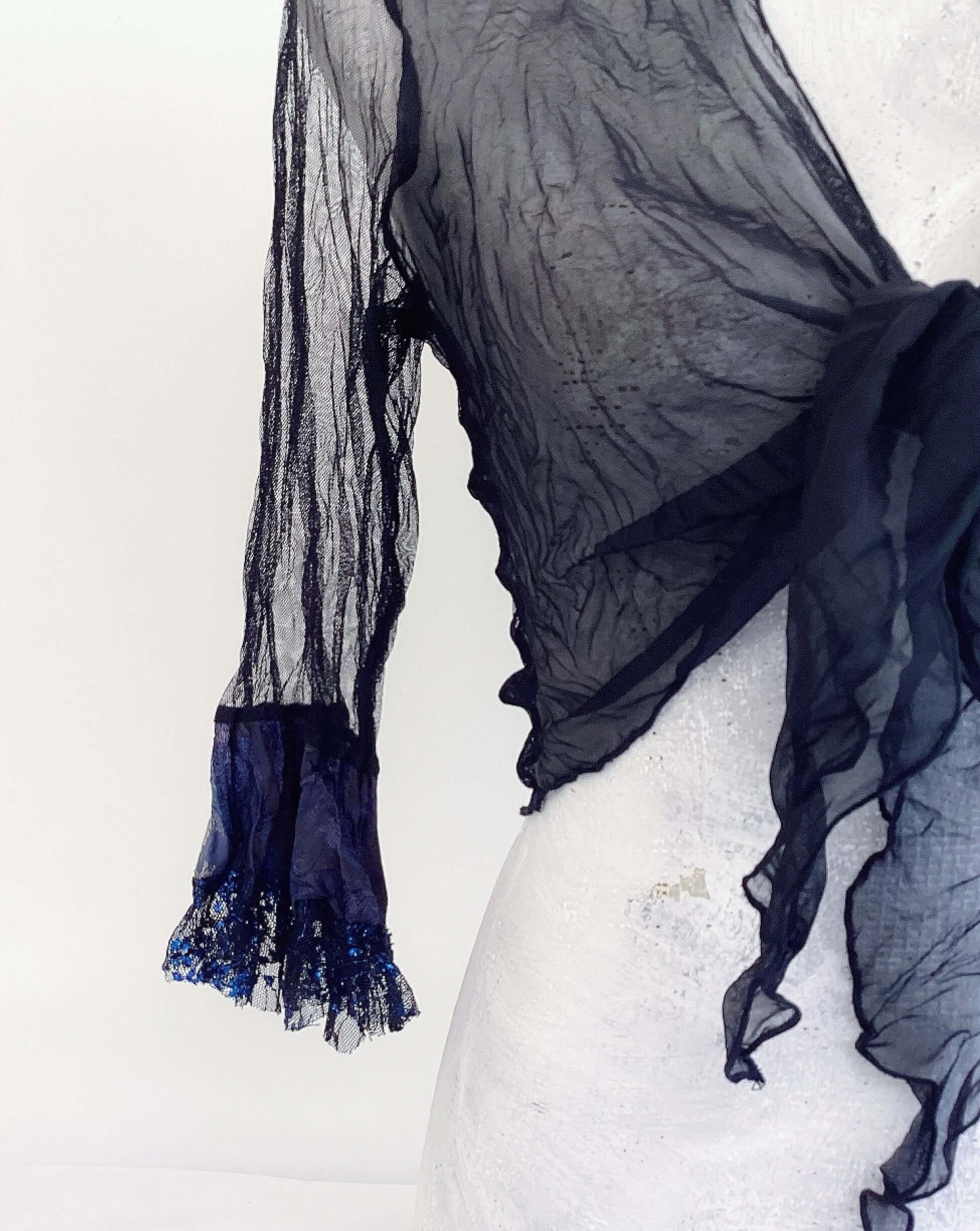 Close up view of tie top, left chiffon front, black net sleeve, black and blue lace cuff.