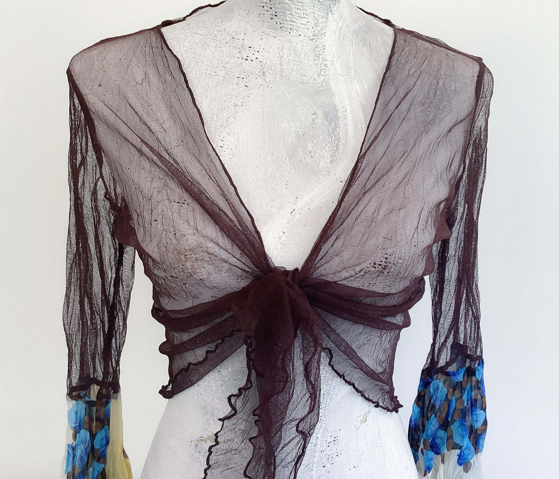 Detail front view of brown net tie top, tied in a knot at the front, with blue rose floral sleeves.