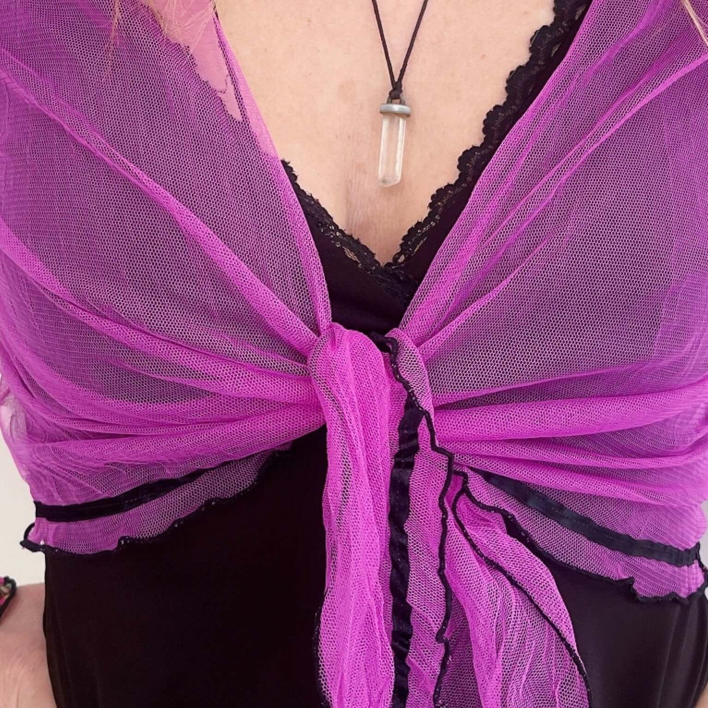Detail view of fuchsia net tie top, tied in the center, black rolled hem, black ribbon along hem.