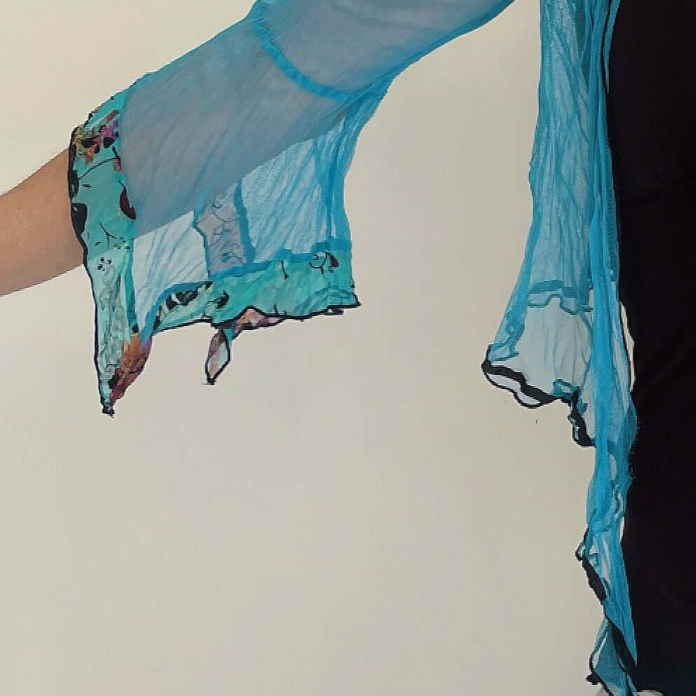 Detail view of turquoise net sleeve, with aqua flocked chiffon on sleeve frills, arm outstretched.