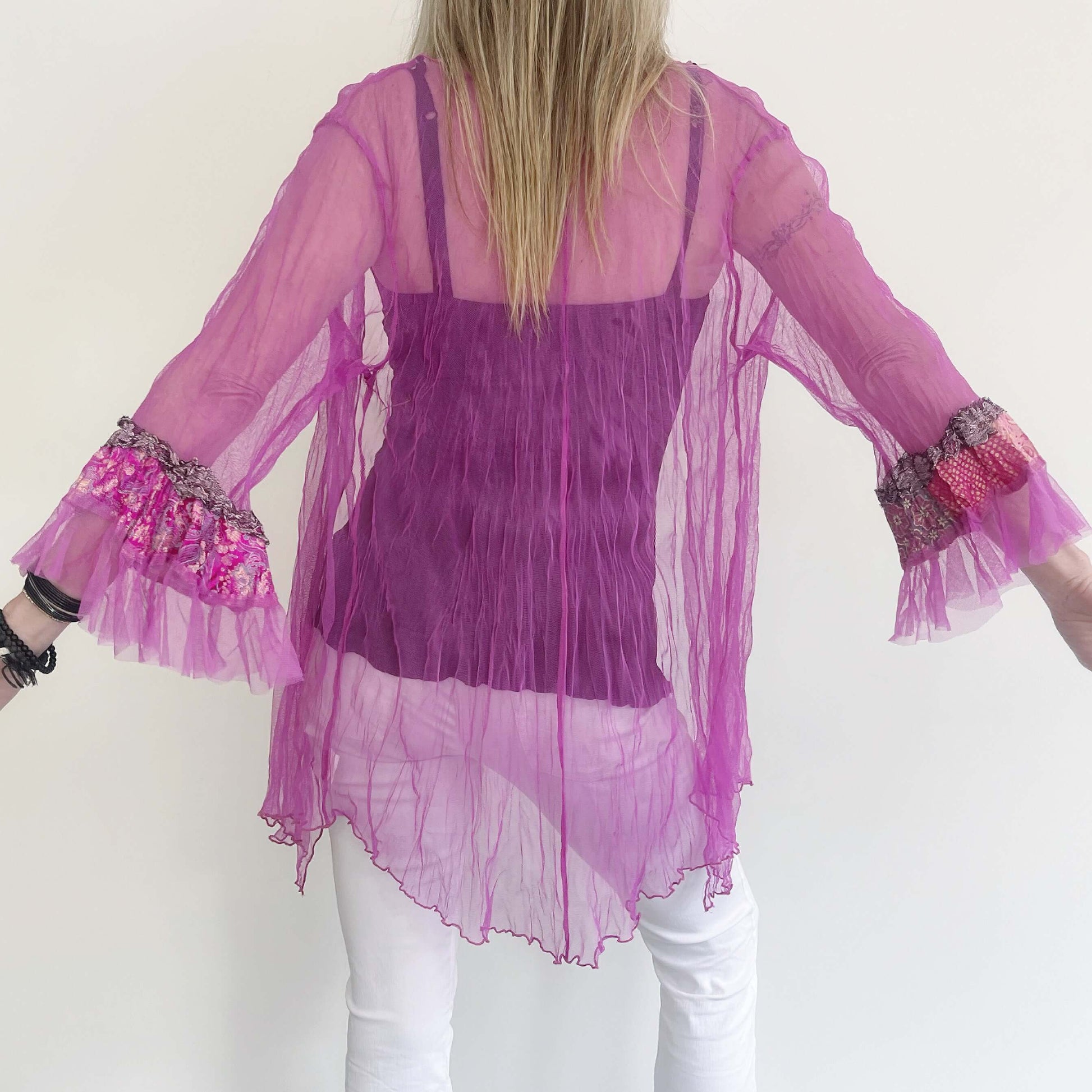 Back view of fuchsia jacket worn loose, model's arms outstretched to show the frilled sleeves. Seam at center.