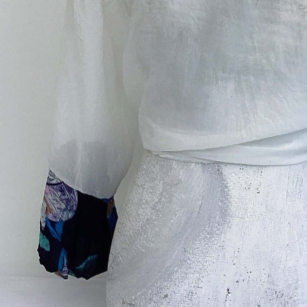 Close up view of off white chiffon tie top, shown from the back, blue floral viscose cuff.