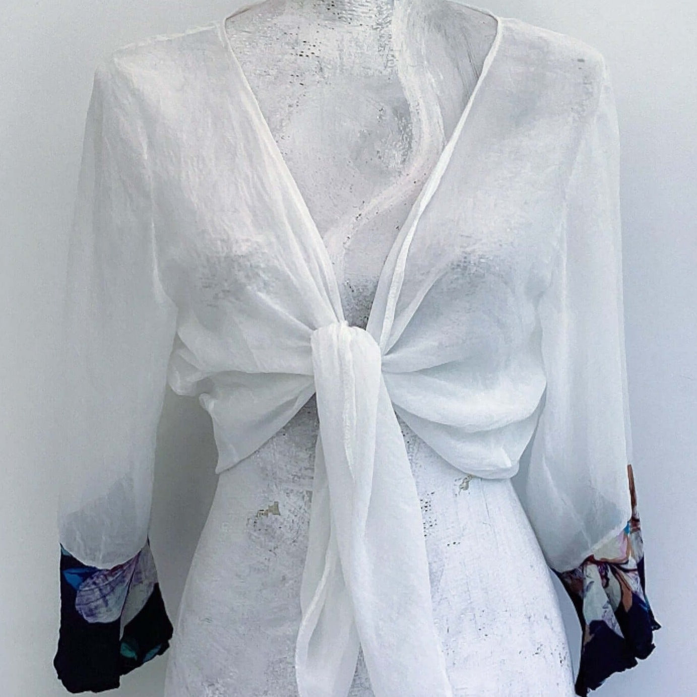 Front view of off white chiffon tie top, knot tied in the center, with blue floral viscose cuffs.