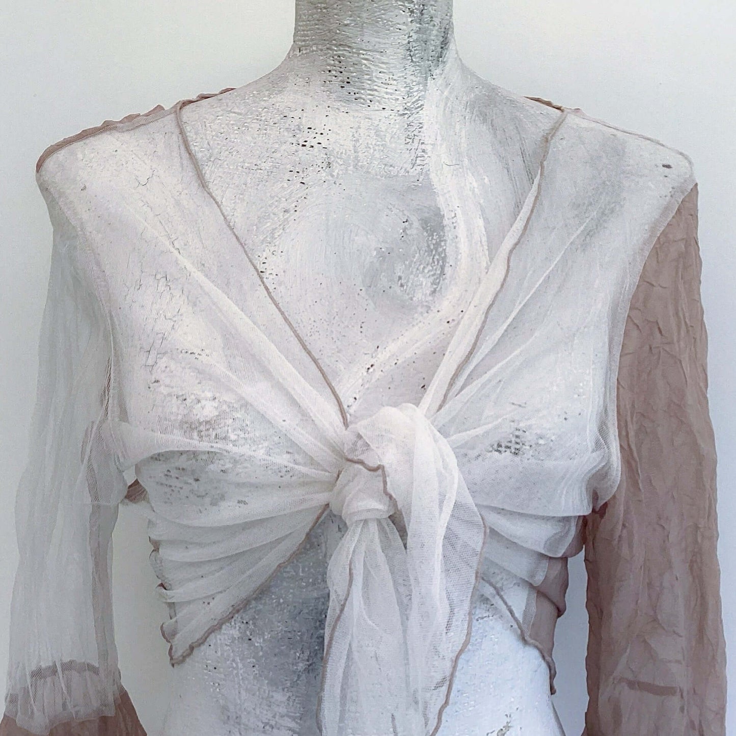 Detail view of tie top, off white net, with biscuit chiffon sleeve on the right, biscuit roll hem.