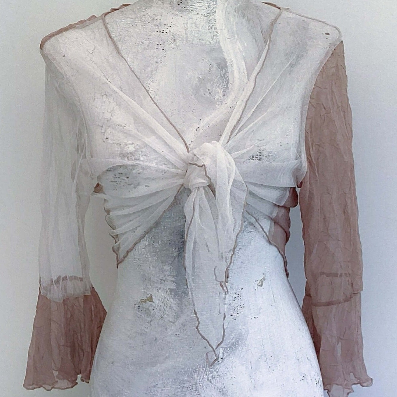 Front view of tie top, off white net, knotted in the center, biscuit chiffon sleeve on the right, biscuit roll hem.