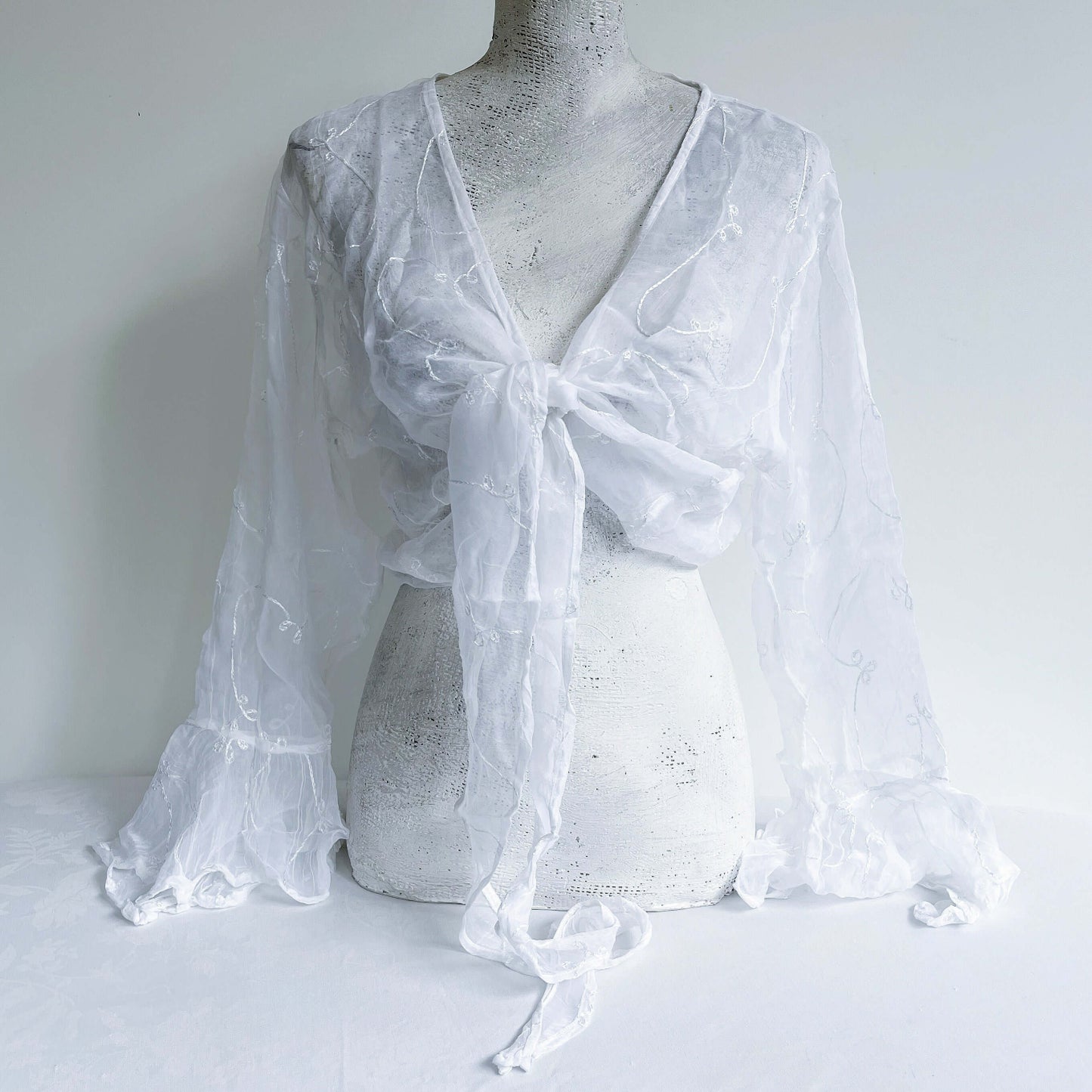 Front view of embroidered chiffon tie top, knotted in the center, long sleeves, flowing frill cuffs.