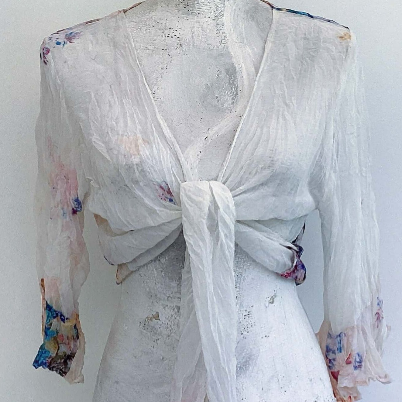 Front view of off white watercolor floral chiffon tie top, knot tied in the center, pale flowers here and there.