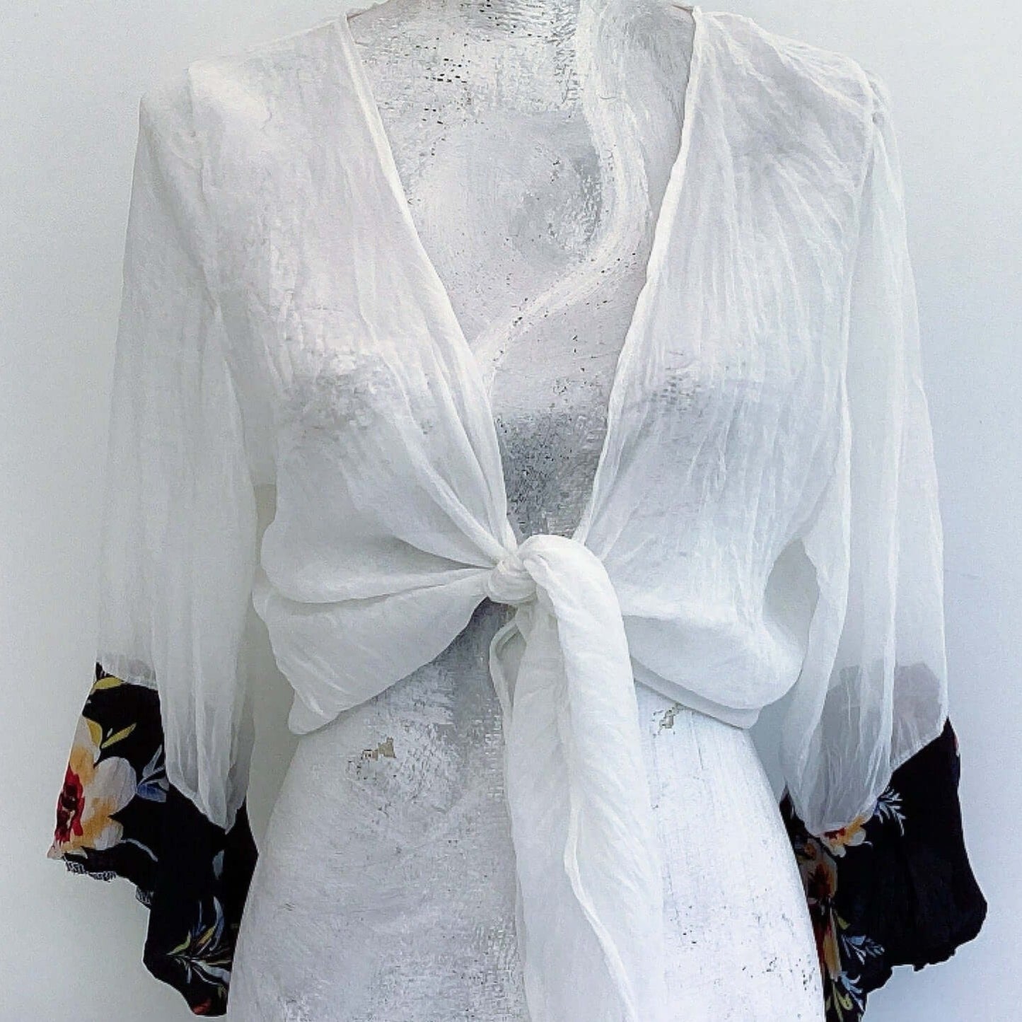 Front view of off white chiffon tie top, knot tied in the center, with red and black floral viscose cuffs.