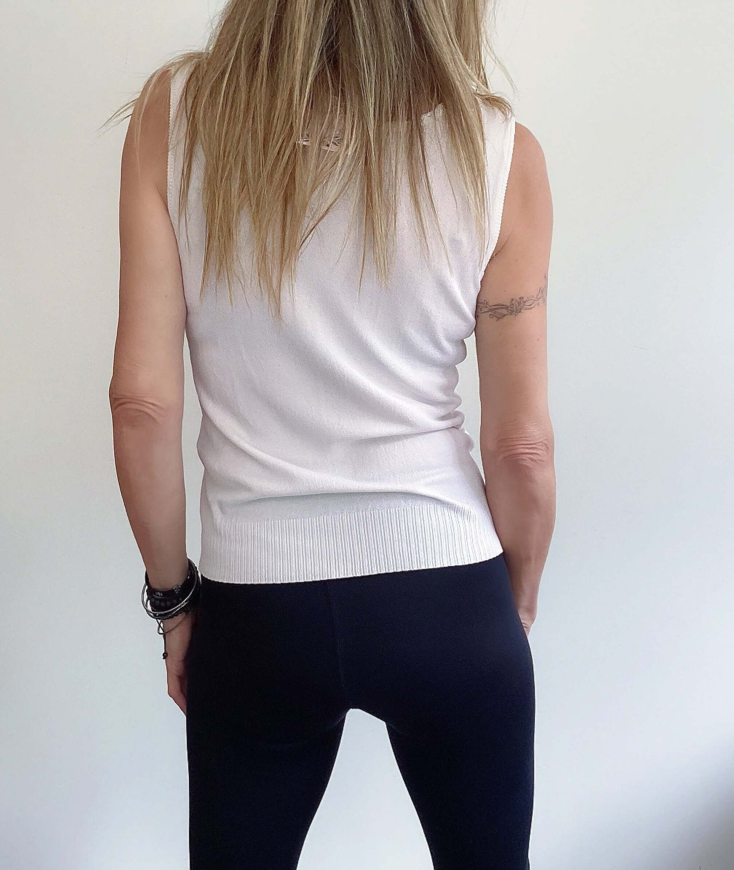 Back view of sleeveless top, scooped neck with string tie, hip length, ribbed at the bottom.