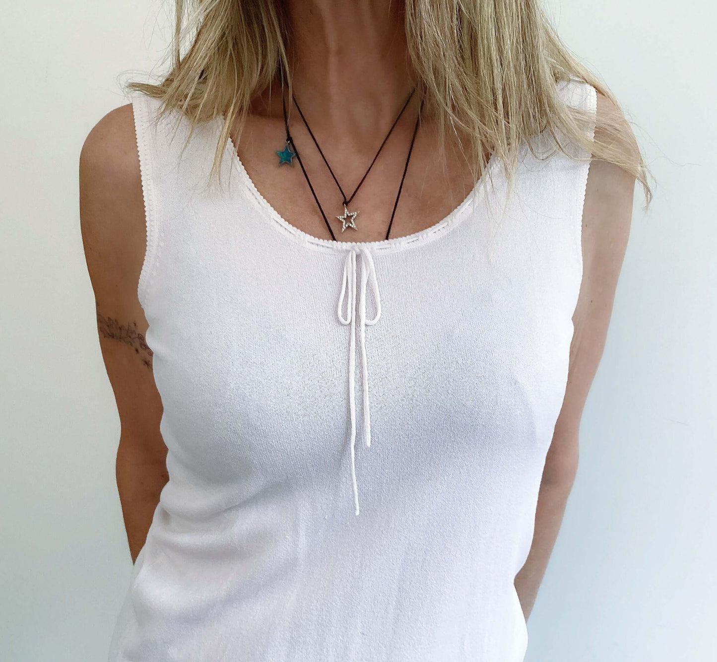 Detail view of sleeveless top, scooped neck with string tie, hip length, ribbed at the bottom.