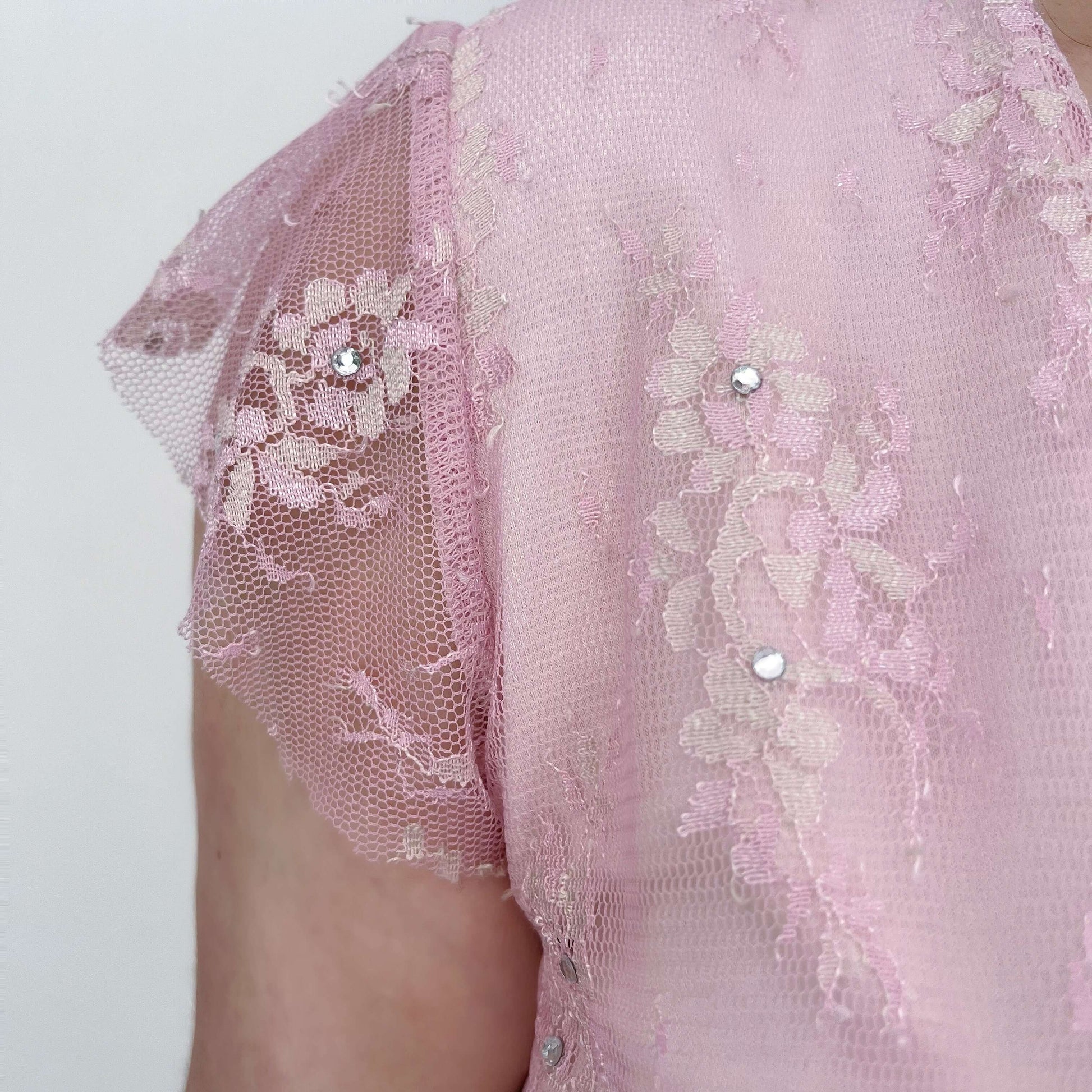 Detail view of swing top tiny capped sleeve, in pink lace with embroidery and crystals.