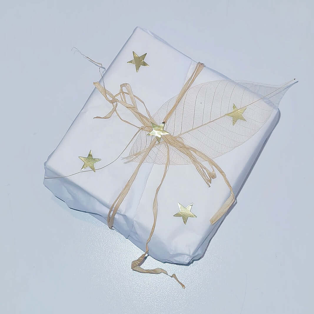 View of box packaging, white tissue paper with raffia ribbon and sticky metallic stars stuck here and there.