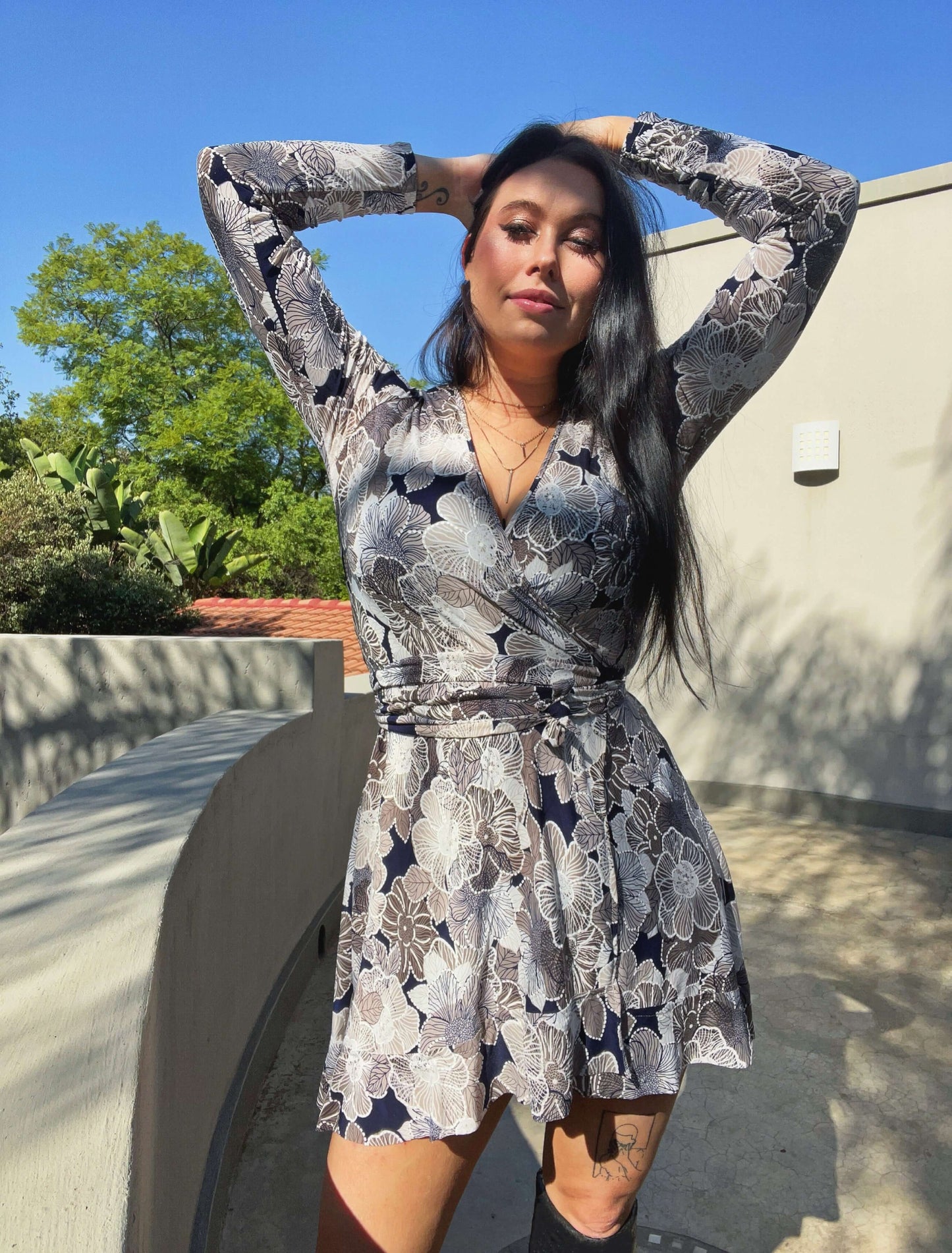 Front view of wrap dress, model with hands above her head, trees and sky in the background.